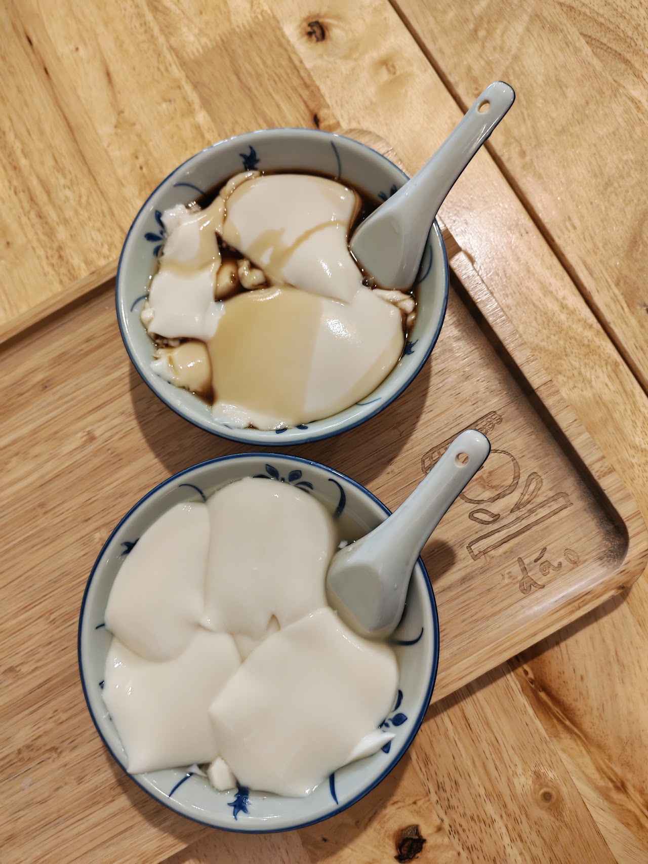 Two bowls of dáo beancurd on a wooden serving tray branded with the dáo name