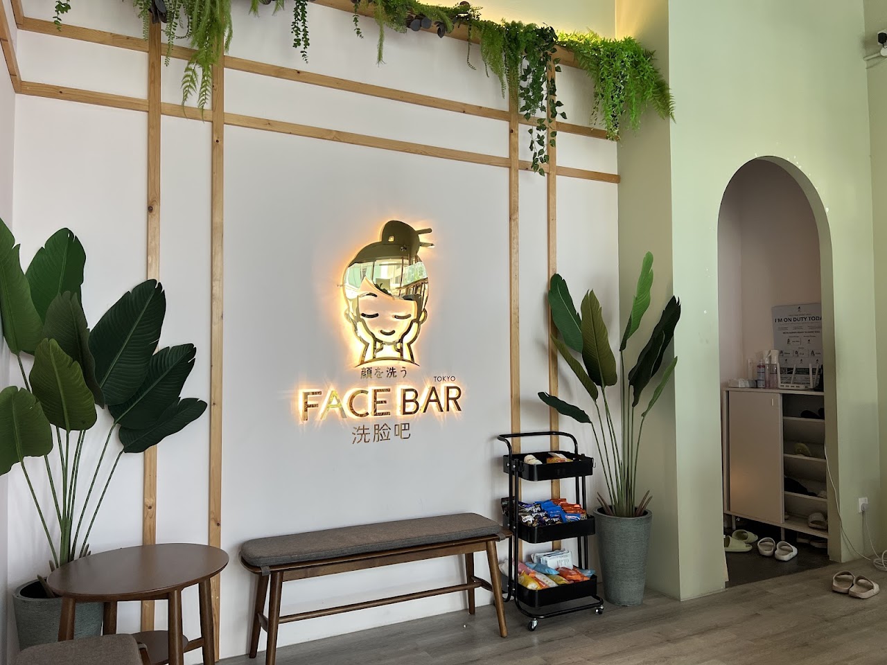 Illuminated Face Bar signage with the brand's face-washing mascot, framed by timber slats and greenery