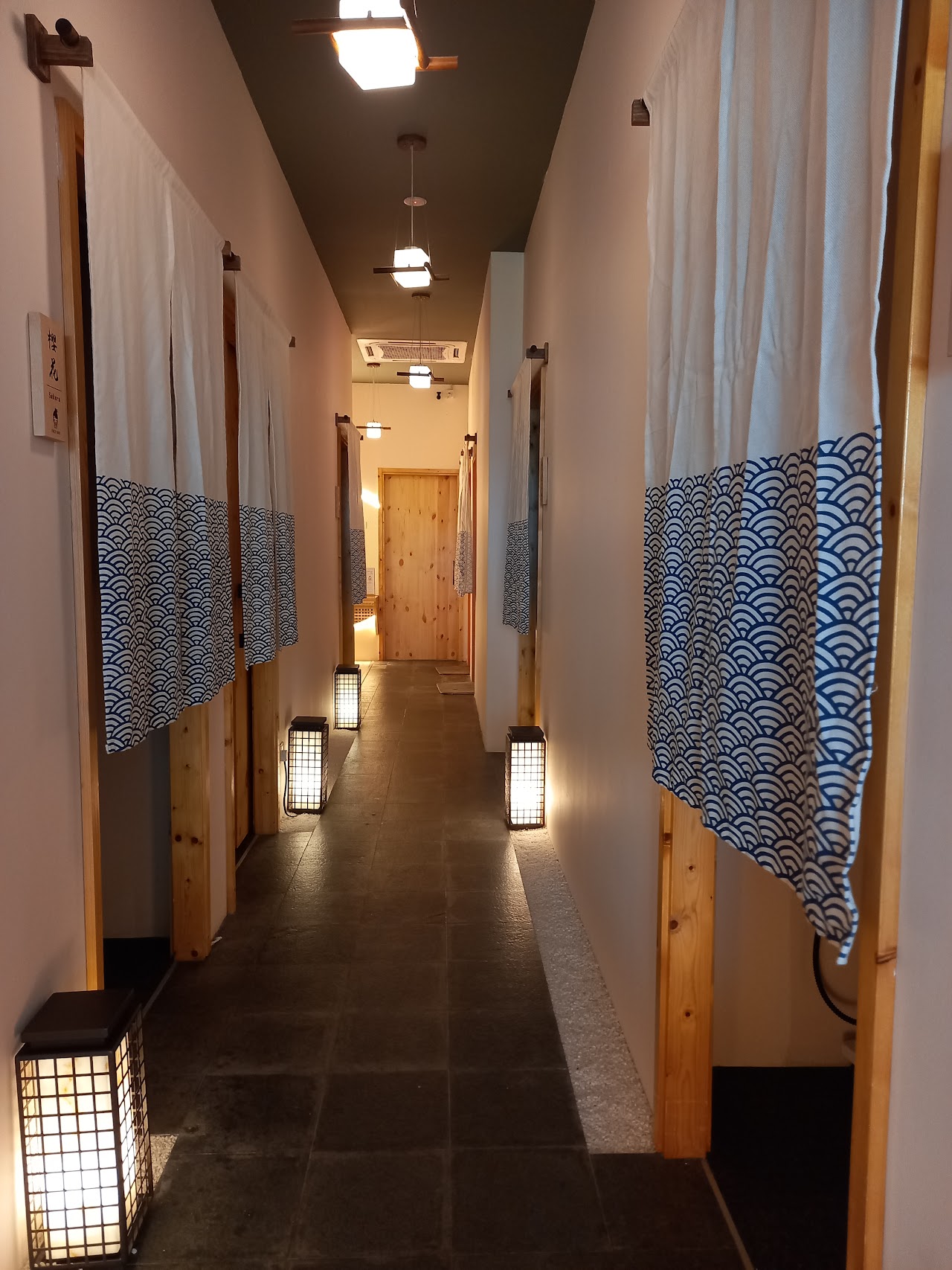 Corridor of curtained treatment rooms at Face Bar Bukit Jalil, seigaiha-print noren and lantern lighting