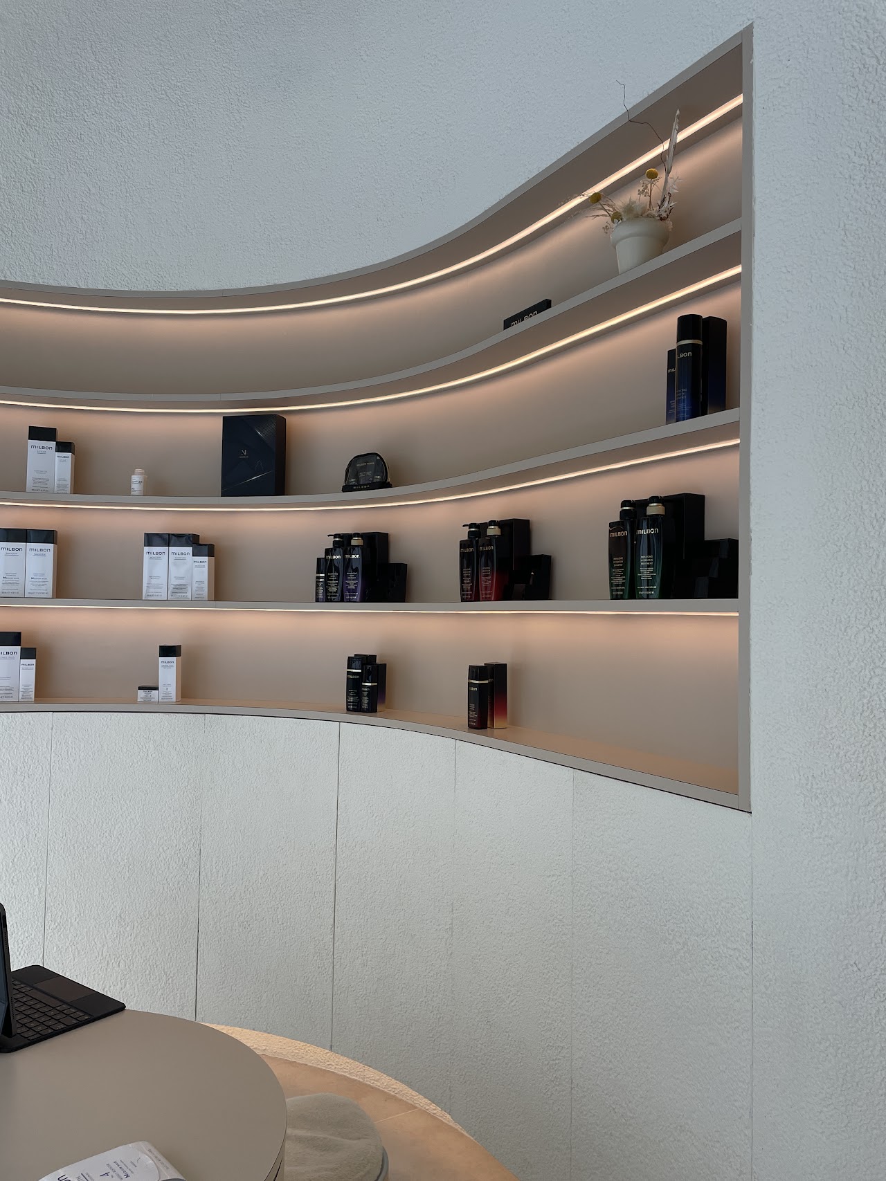 Backlit curved shelving displaying Milbon haircare products
